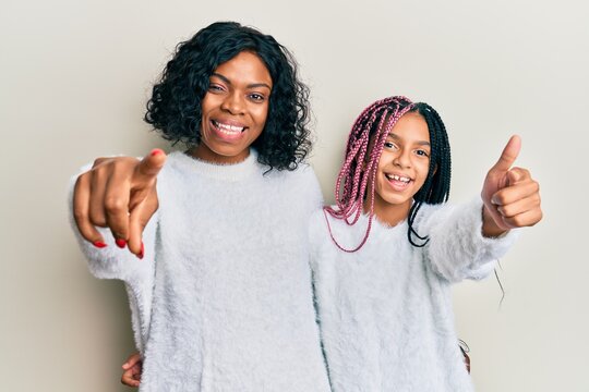 Beautiful african american mother and daughter wearing casual winter sweater pointing fingers to camera with happy and funny face. good energy and vibes.