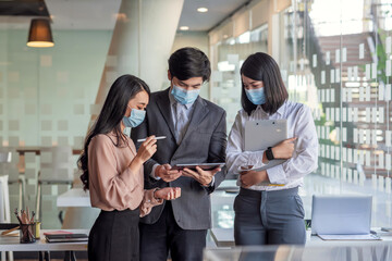 Fototapeta na wymiar Team Asian businesswoman and businessman stand consult the idea of ​​working together using a tablet to wear a mask to prevent germs.at the office.
