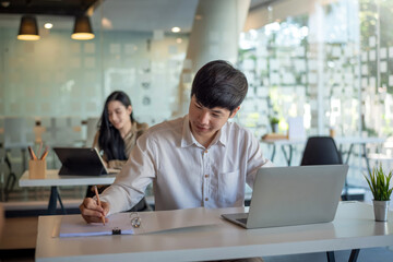 Asian businessman is working at the office holding a pencil and a laptop at his desk the back blurred at the office.