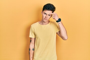Young hispanic man wearing casual yellow t shirt pointing unhappy to pimple on forehead, ugly...