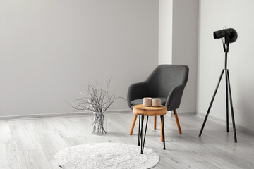 Modern armchair with table, lamp and vase near light wall in room