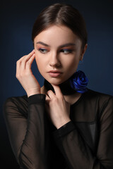 Beautiful young woman with blue rose on dark background