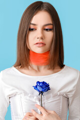 Beautiful young woman with blue rose on color background