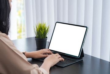 Side view of a businesswoman typing a work on a tablet blank white screen at the desk. Mock up.