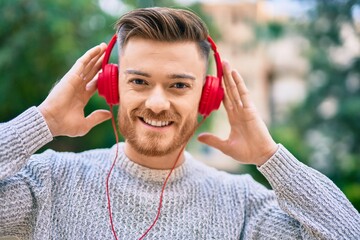 Young caucasian man smiling happy listening to music using headphones at the park.