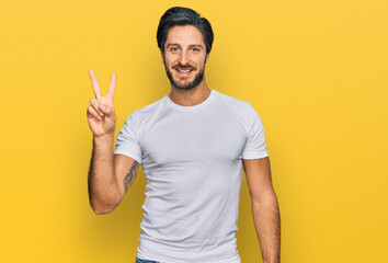 Young hispanic man wearing casual white t shirt showing and pointing up with fingers number two while smiling confident and happy.