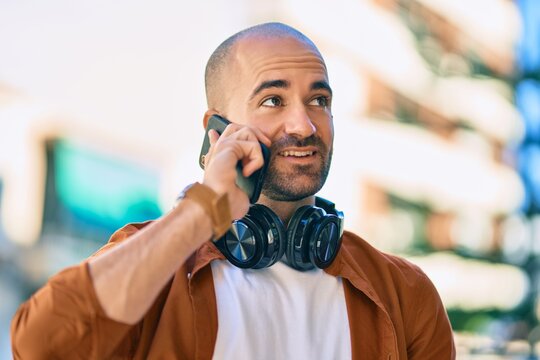 Young hispanic bald man smiling happy talking on the smartphone using headphones at the city.