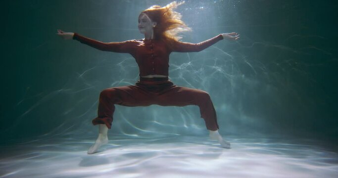 Cinematic shot of young beautiful fun happy active redhead woman doing fun crab dance moves under water slow motion.