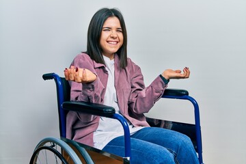 Young brunette woman sitting on wheelchair smiling cheerful with open arms as friendly welcome,...