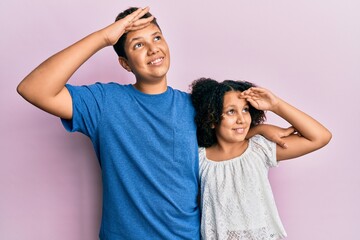 Young hispanic family of brother and sister wearing casual clothes together very happy and smiling looking far away with hand over head. searching concept.