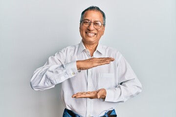 Middle age indian man wearing casual clothes and glasses gesturing with hands showing big and large size sign, measure symbol. smiling looking at the camera. measuring concept.