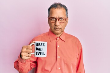Middle age indian man drinking mug of coffee with best dad ever message thinking attitude and sober...