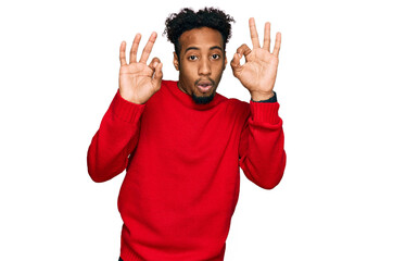 Young african american man with beard wearing casual winter sweater looking surprised and shocked doing ok approval symbol with fingers. crazy expression