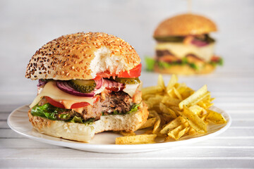 Homemade burger close-up with juicy beef patty, tomatoes, sauce, lettuce, onions,pickles, potato chips on a light wooden background. Fast food. Horizontal orientation, no people.