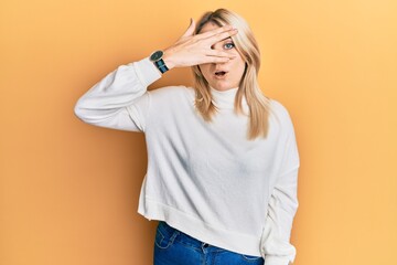 Young caucasian woman wearing casual winter sweater peeking in shock covering face and eyes with...