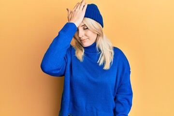 Young caucasian woman wearing wool winter sweater and cap surprised with hand on head for mistake,...