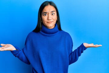 Young asian woman wearing casual winter sweater clueless and confused with open arms, no idea concept. - obrazy, fototapety, plakaty