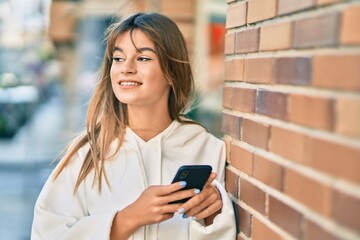Caucasian sporty teenager girl smiling happy using smartphone at the city.