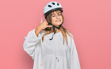 Teenager caucasian girl wearing bike helmet smiling doing phone gesture with hand and fingers like talking on the telephone. communicating concepts.