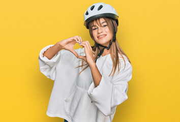 Teenager caucasian girl wearing bike helmet smiling in love doing heart symbol shape with hands. romantic concept.