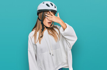 Teenager caucasian girl wearing bike helmet peeking in shock covering face and eyes with hand, looking through fingers with embarrassed expression.