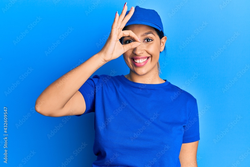 Poster beautiful brunette woman wearing delivery uniform smiling happy doing ok sign with hand on eye looki