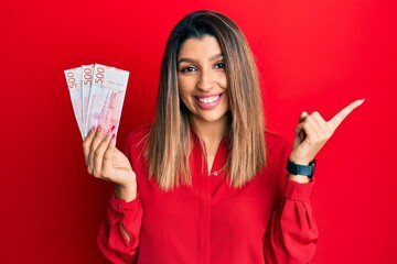 Beautiful brunette woman holding 500 swedish krona banknotes smiling happy pointing with hand and finger to the side