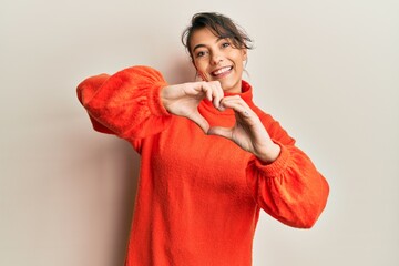 Young hispanic woman wearing casual winter sweater smiling in love doing heart symbol shape with hands. romantic concept.