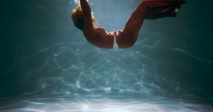 Cinematic side view of young beautiful woman slowly sinking deep under water. Depression, loneliness concept slow motion