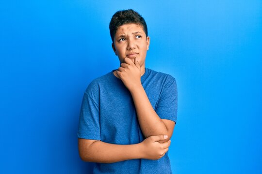 Teenager hispanic boy wearing casual blue t shirt thinking concentrated about doubt with finger on chin and looking up wondering
