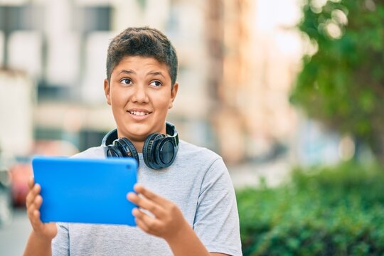 Adorable latin boy smiling happy using headphones and touchpad at the park.