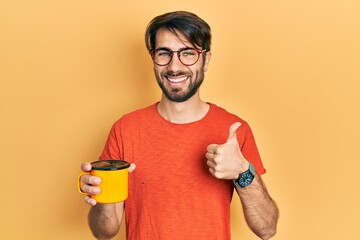 Young hispanic man drinking a cup of coffee smiling happy and positive, thumb up doing excellent and approval sign