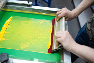 Fototapeta na wymiar Serigraphy silk screen print process at clothes factory. Frame, squeegee and plastisol color paints.