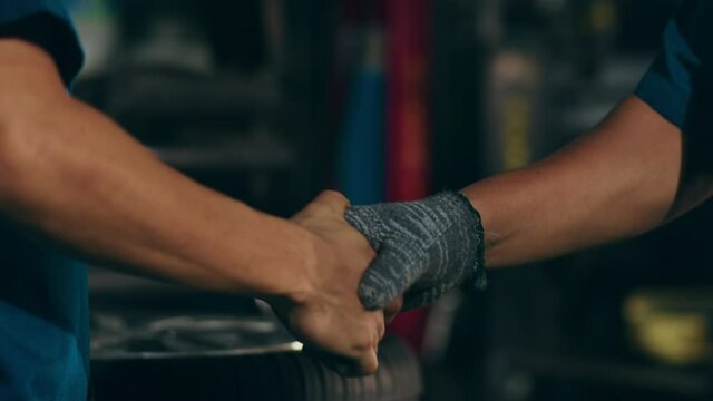 Professional car mechanic shaking hands with the car service client at repair service station. Wheel alignment work at workshop night. Skillful Asian guy in uniform fixing car. Car service repair.