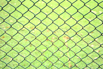 Old chain link pattern abstract fence with green grass field background. Focus foreground with soft, blurry background. Any backdrop, private property, prison, entrance, sports or game field concept.