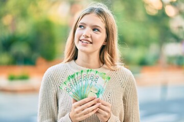 Beautiful caucasian teenager smiling happy holding russian 200 ruble banknotes at the city.