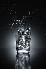 Glass of water with artistic splash, generated by ice cubes composed on black background with lighting 