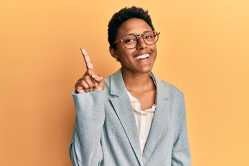 Young african american girl wearing business jacket and glasses showing and pointing up with finger...
