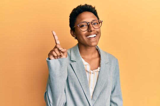 Young african american girl wearing business jacket and glasses showing and pointing up with finger number one while smiling confident and happy.