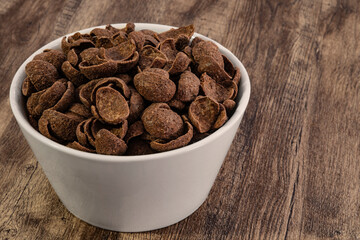 chocolate cereals in white bowl on wood background.