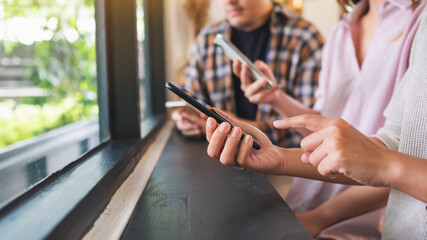 Obraz premium Group of young people holding and using their mobile phones while sitting together