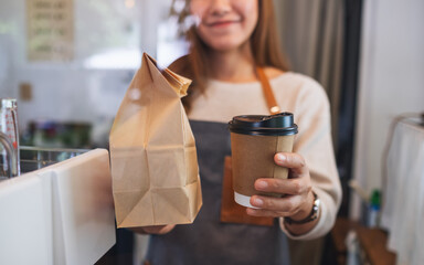 Closeup image of a waitress holding and serving paper cup of coffee and takeaway food in paper bag...