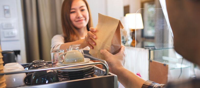 A waitress holding and serving a takeaway food in paper bag to customer in a shop