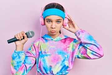 Young brunette girl singing song using microphone wearing sportswear depressed and worry for distress, crying angry and afraid. sad expression.