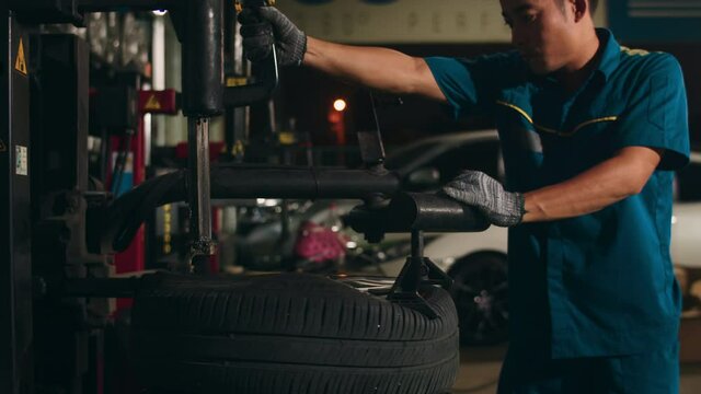 Professional car mechanic changing a car tire on lifted automobile at repair service station. Wheel alignment work at workshop night. Skillful Asian guy in uniform fixing car. Car service repair.