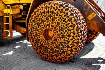 Yellow metal chains with sandy dirt on huge tire of construction machine. Chains with ring chain links closeup. Grungy rough chains closeup. Construction industrial skidder. Industrial tractor wheels