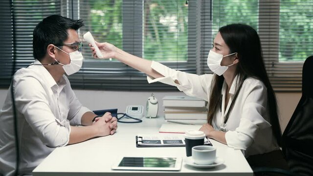 Medium close up shot of the Asian woman doctor and patient wearing surgical mask during examination or temperature checking, Healthcare concept between medical people and patient in workplace area. 