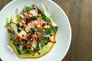 Vegetarian salad bowl with avocado mousse, parmesan cheese, spinach, berry sauce and baked apples in a plate on a wooden background. Healthy and dietary food
