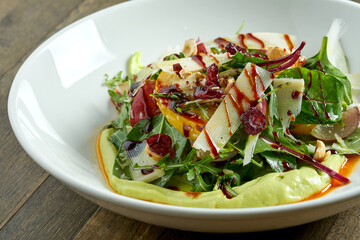 Vegetarian salad bowl with avocado mousse, parmesan cheese, spinach, berry sauce and baked apples in a plate on a wooden background. Healthy and dietary food