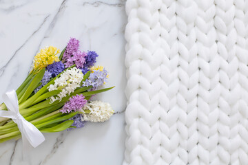 Bouquet of spring colored flowers of hyacinths. White marble background and fluffy knitted plaid